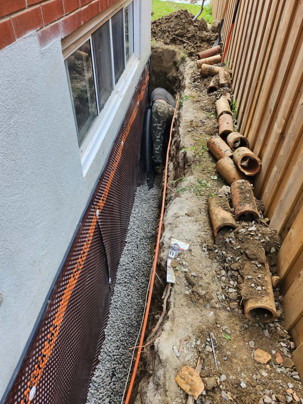 Crew member installing new drainage pipe with the old clay tile stacked beside the trench