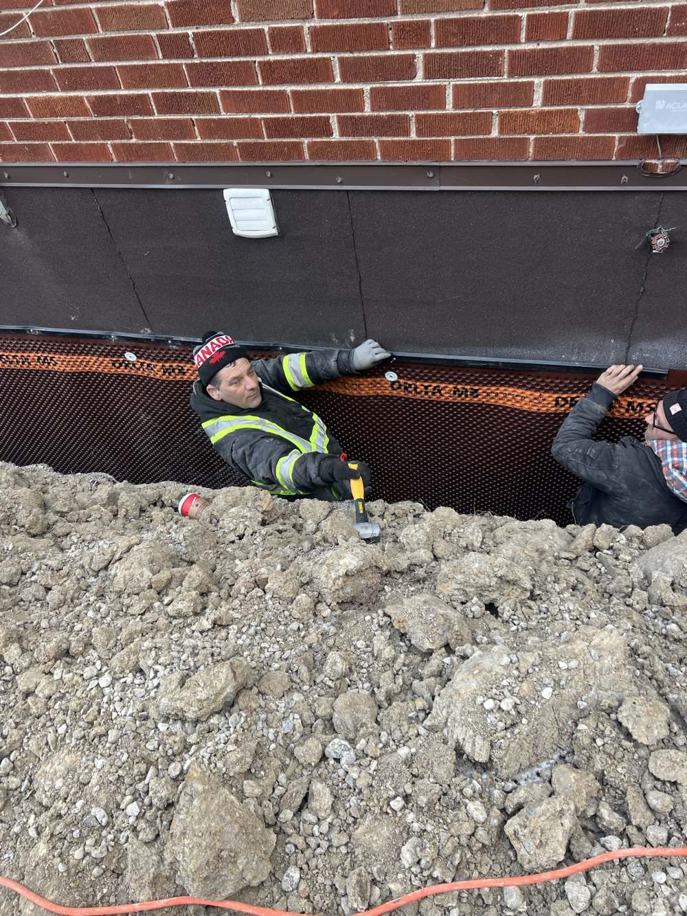Two crew members fastening the top rail of the foundation membrane in winter conditions
